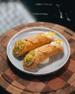 Deux cannoli siciliani garnis de crème de ricotta, extrémités aux pistaches concassées et zeste de citron