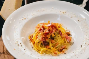 Spaghetti carbonara au guanciale dans une assiette creuse blanche bordée de pecorino râpé