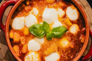 Gnocchi alla sorrentina gratinés dans une cocotte rouge, avec billes de mozzarella fondue et feuilles de basilic