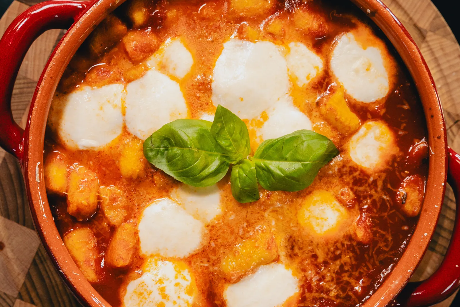 Gnocchi alla sorrentina gratinés dans une cocotte rouge, avec billes de mozzarella fondue et feuilles de basilic