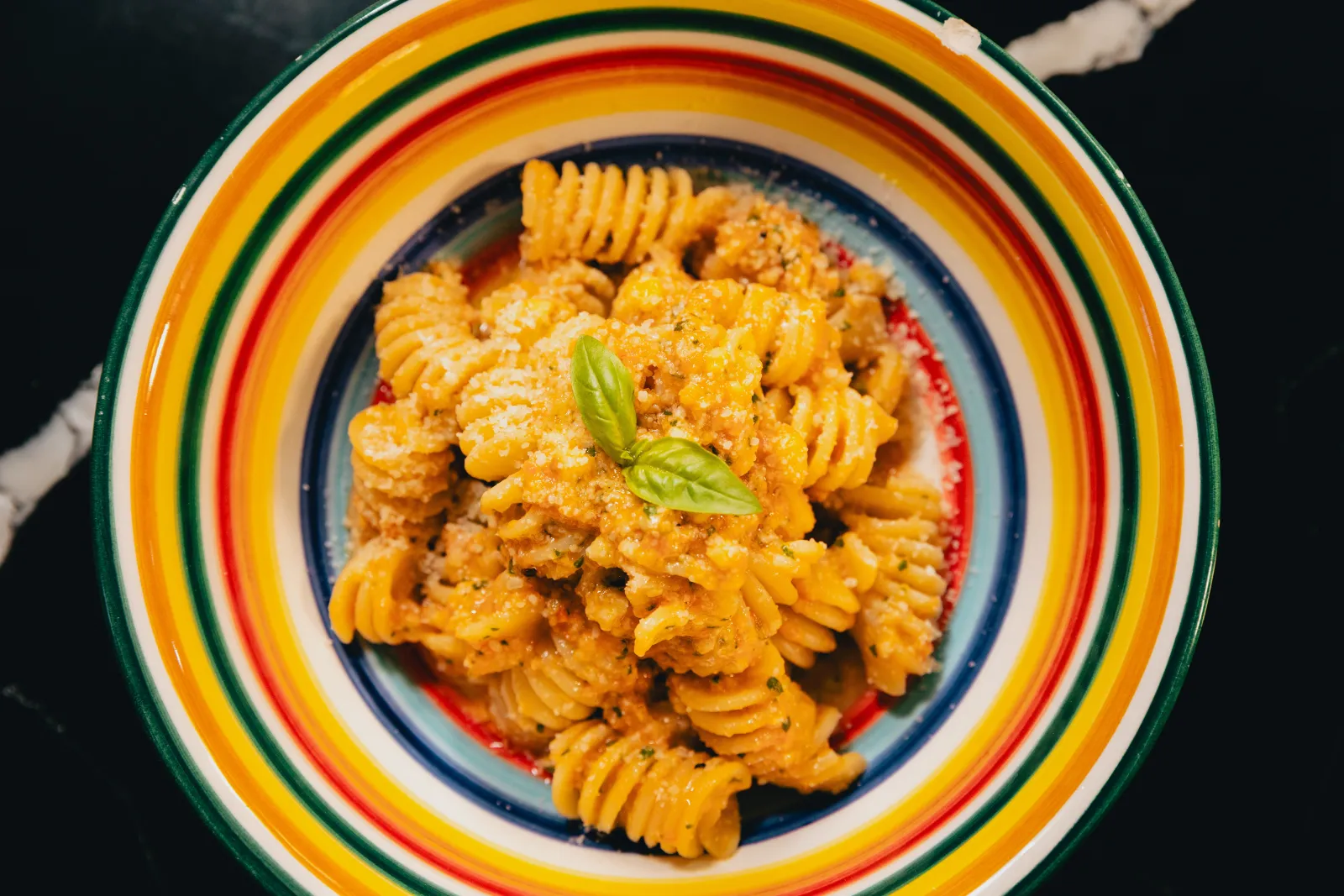 Gros fusilli au pesto alla trapanese dans une assiette à rayures colorées, avec une feuille de basilic