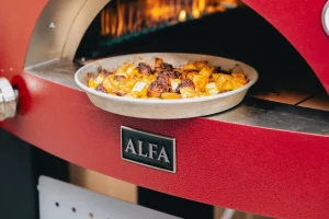 Plat en aluminium de pommes de terre dorées et morceaux de saucisse grillée à la sortie d'un four rouge