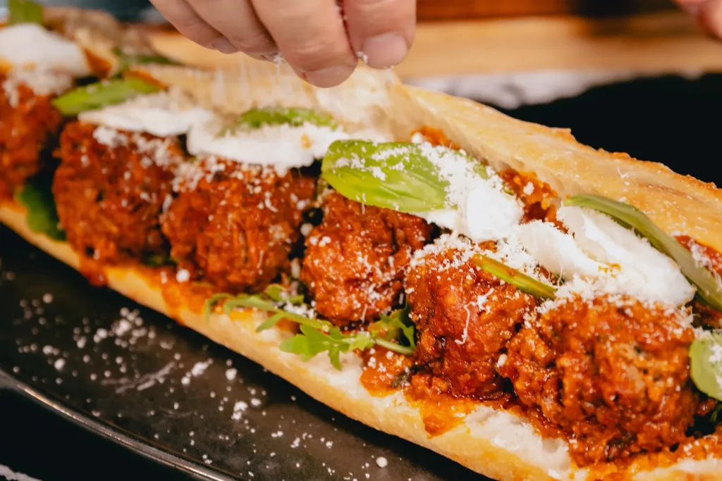 Baguette ouverte garnie de polpette à la sauce tomate, roquette, mozzarella, basilic et parmesan râpé
