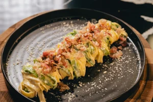 Nid de tagliatelle jaunes et vertes à la crème, garni de pancetta croustillante et de parmesan, sur une assiette noire